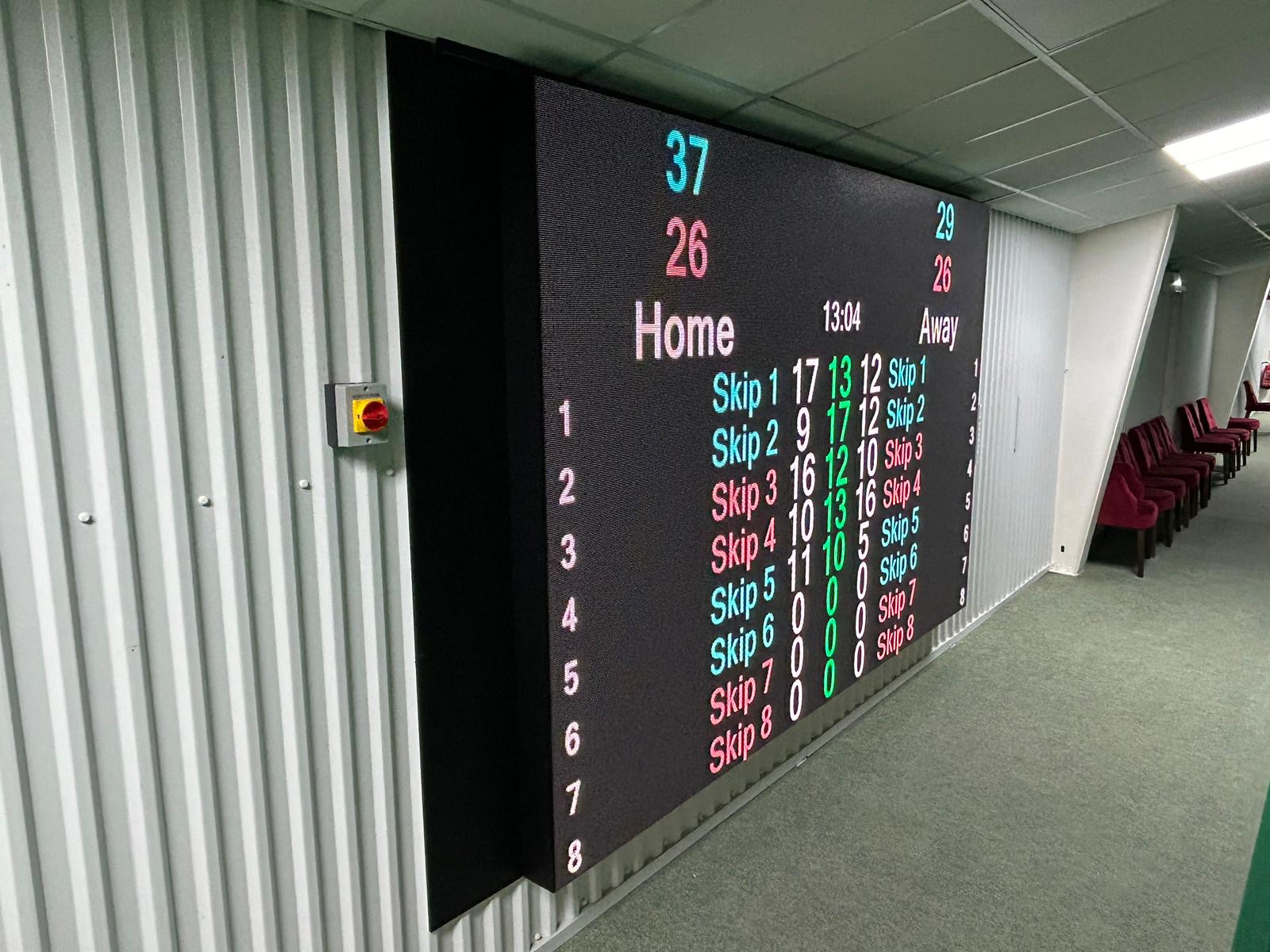 Indoor video screen showing cricket scoring information
